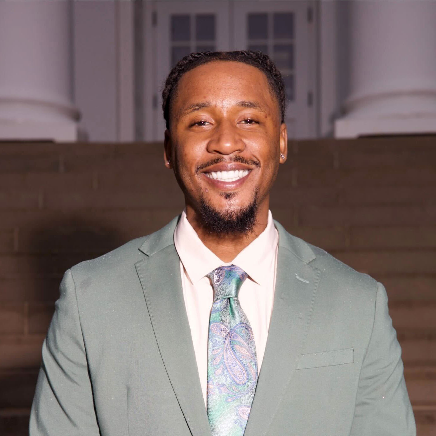A headshot of a Black man wearing a light gray suit.